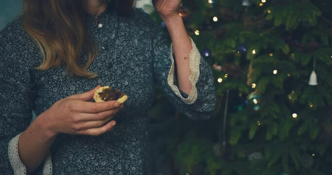 A young woman is enjoying a mince pie and a hot drink by the christmas tree