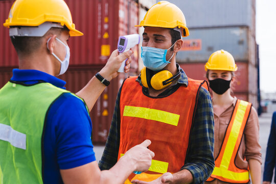 Worker scanning fever temperature with digital thermometer to construction site staff wearing hygiene face mask protect from Coronavirus or COVID-19. New Normal working life adaptation in 2020