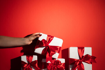 Christmas gift. Holiday sale. Female hand picking up choosing present from stack with white wrapped boxes isolated on red copy space background. Happy New Year. Special offer.