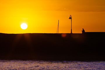 Skyline of a sunset on the pier with person sitting watching the sunset