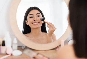 Happy pretty asian woman applying blush on her face