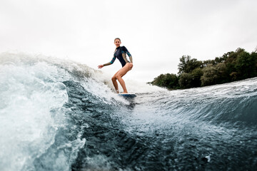 Fototapeta premium Smiling woman in wetsuit rides down on surf style wakeboard on wave