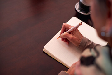 Close Up Of Senior Woman At Home Sitting At Table And Writing In Notebook Or Journal