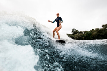 woman in wetsuit rides on wakesurf down on huge splashing river wave