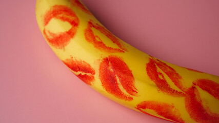 Red lipstick on a yellow banana on a pink background. Love and sex concept.