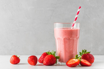 Strawberry smoothie or milkshake in a glass with a straw and fresh berries on white background....