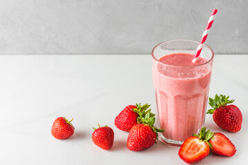 Strawberry milkshake or smoothie in a glass with a straw and fresh berries on white background. Summer drink