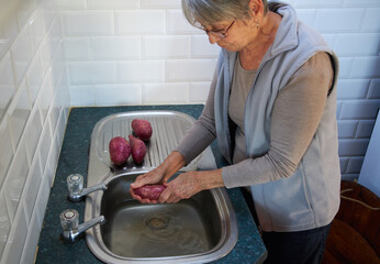 Senior Woman Preparing Vegetables Washing Potatoes In Kitchen Sink At Home