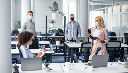 Meeting with boss. Young business woman in protective mask gives task, african american woman makes...