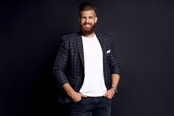 Obraz premium Confident and handsome. Young man with ginger beard in smart-casual clothes smiling looking at camera while posing against black background