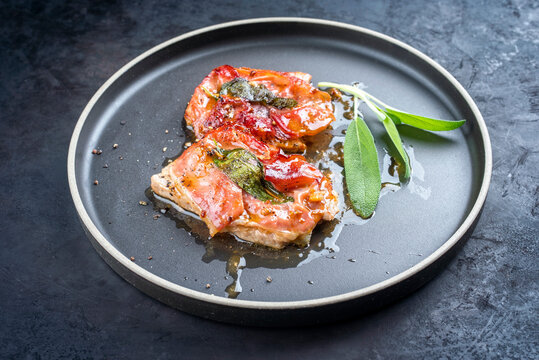 Modern style traditional Italian fried pork saltimbocca alla Romana with Parma ham and sage leaves offered as close-up in a Nordic design plate