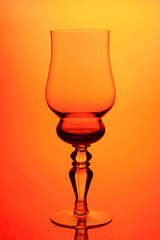 Transparent glass wine glass on orange background