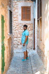 Young adult man stands on an alley in Valldemossa wearing blue shoes and shirt while looking at camera