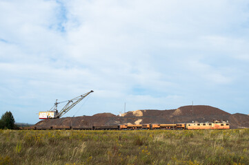 Fototapeta premium A large walking excavator forms dumps of rock delivered by freight train from a mining quarry. Background