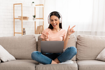 Obraz premium Woman listening to music in headphones on couch, using pc