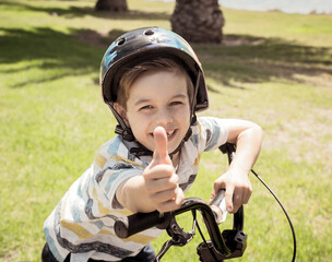 Fototapeta na wymiar Portrait of cheerful cute kid with helmet riding his bike at the park