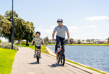 Obraz premium Father and son riding their bikes having fun together in the park by the lake
