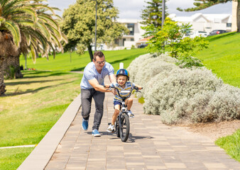 Obraz premium Father teaching his son to ride a bike and having fun together at the park