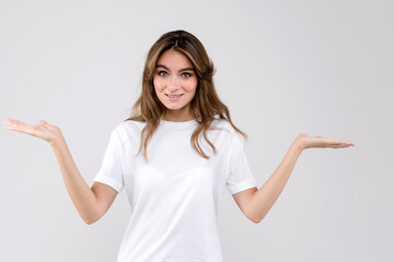 Atrractive young woman wearing white t-shirt isolated over white background showing confused expression with arms and hands raised. Doubt concept
