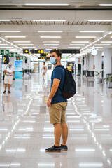 Young man wearing a protective mask stands in the middle of an airport terminal
