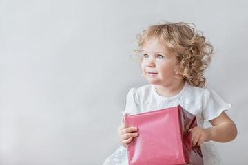 Happy girl in white dress with Christmas gift on light gray background 