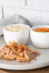 Pulled pork with rice and vegetables on a grey plate.  Grey brick background with a tea towel
