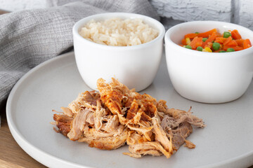 Pulled pork with rice and vegetables on a grey plate.  Grey brick background with a tea towel