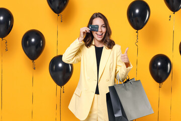 Funny young woman in suit jacket hold package bags with purchases after shopping covering eye with...