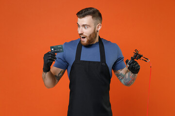 Shocked professional tattooer master artist tattooed man in apron hold credit bank card machine...