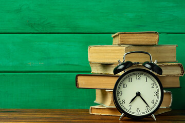 Education concept. Black vintage alarm clock with old books on the table.