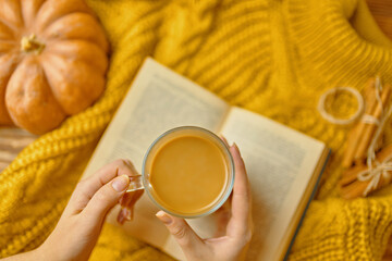 Top view of girl's hand on a table,a pumpkin, cinnamon sticks, a book on wooden table. Cozy knitted warm orange sweater. Seasonal background, autumn theme, wooden textured table. 