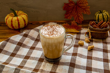 Pumpkin spice coffee with whipped cream and seasonal autumn decoration. Cinnamon sticks and decorative little pumpkins.