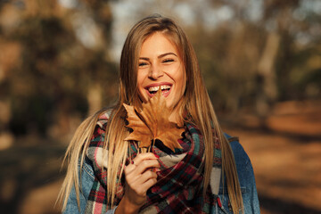Portrait of a beautiful blonde with a smile on face holding a leaf in hand in the park