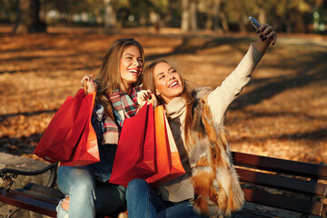 Two women friends taking a selfie in park after shopping - obrazy, fototapety, plakaty