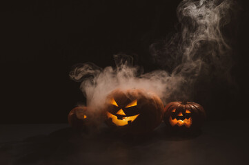 Three creepy halloween steaming pumpkins with a carved luminous smirk on a black background. A...