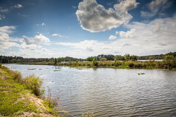 View of a large piece of land in the country with a cabin on it as well as a large fishing pond and taken on a bright and summy day