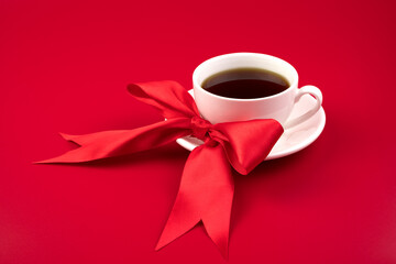 Beautiful composition with a white Cup and a red satin bow on a red background. Romantic background. The concept of the cards, a meeting of lovers.