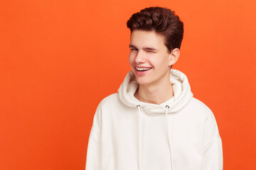 Handsome guy in white sweater with stylish hairdo winking and optimistically smiling, good mood....