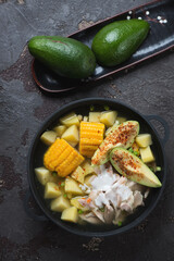 Cast-iron pan with colombian traditional ajiaco soup, vertical shot on a brown stone background, top view