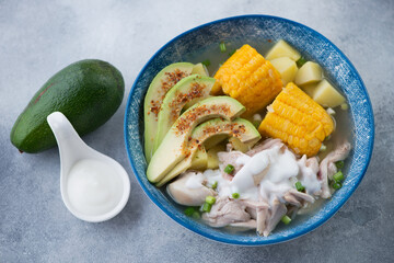 Blue plate with ajiaco or colombian potato, chicken and corn stew, studio shot on a light-blue stone background