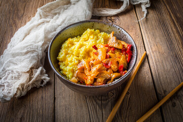 Saffron rice with pieces of chicken and vegetables on wooden table.