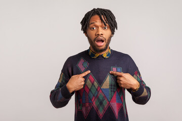 Extremely surprised shocked african man with dreadlocks pointing fingers at himself with widely...