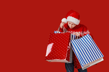 Cute boy in red sweater holding shopping bags with Christmas gifts .