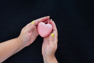 female hands holding a pink heart on a black background. copy space..