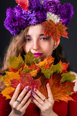 Autumn girl nymph with a bright headdress of flowers and with maple leaves in her hands