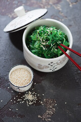 Bowl of seaweed salad with sesame seeds on a brown stone background, vertical shot, selective focus