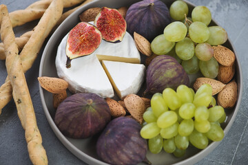 Closeup of camembert cheese, fig fruits, grapes, almonds and salted breadsticks, selective focus