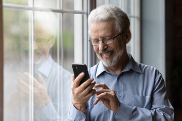 Happy senior Caucasian man in glasses look at cellphone screen browse wireless internet. Smiling...