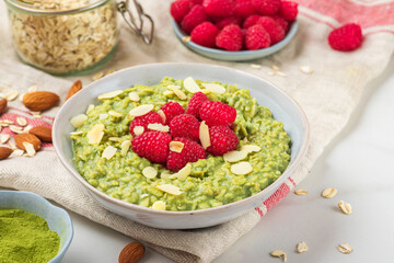 Oatmeal matcha porridge with fresh raspberries and nuts in a bowl for healthy diet breakfast on...