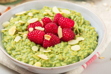 oatmeal porridge with matcha powder, raspberries and nuts in a bowl for healthy diet breakfast on white background